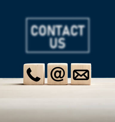 Phone and e-mail icons on wooden cubes with contact us text on blue background. Website page contact us or e-mail marketing concept.